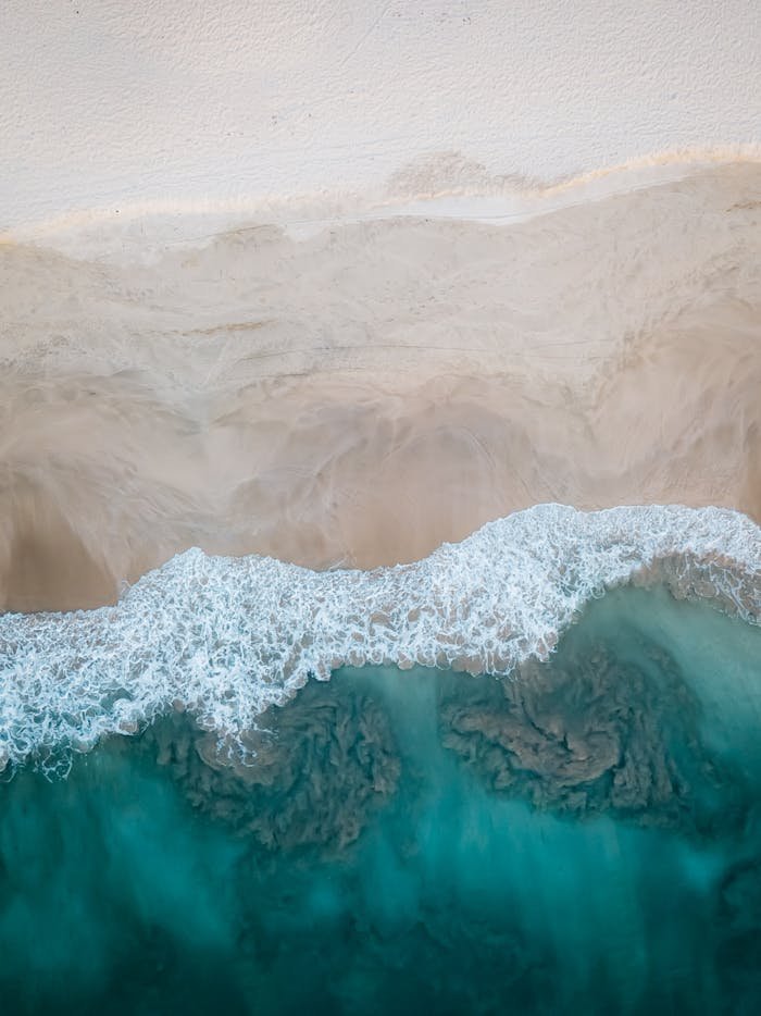 A stunning aerial view showcasing a sandy beach meeting the turquoise ocean waves. Perfect for travel and nature themes.